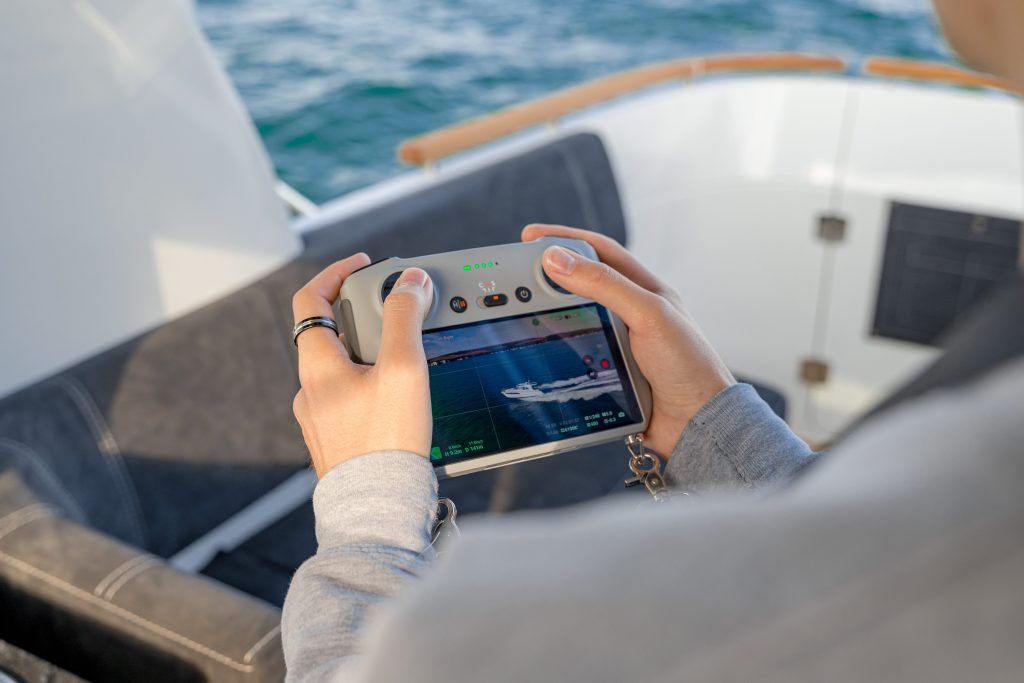 Male hands operating drone filming moving boat
