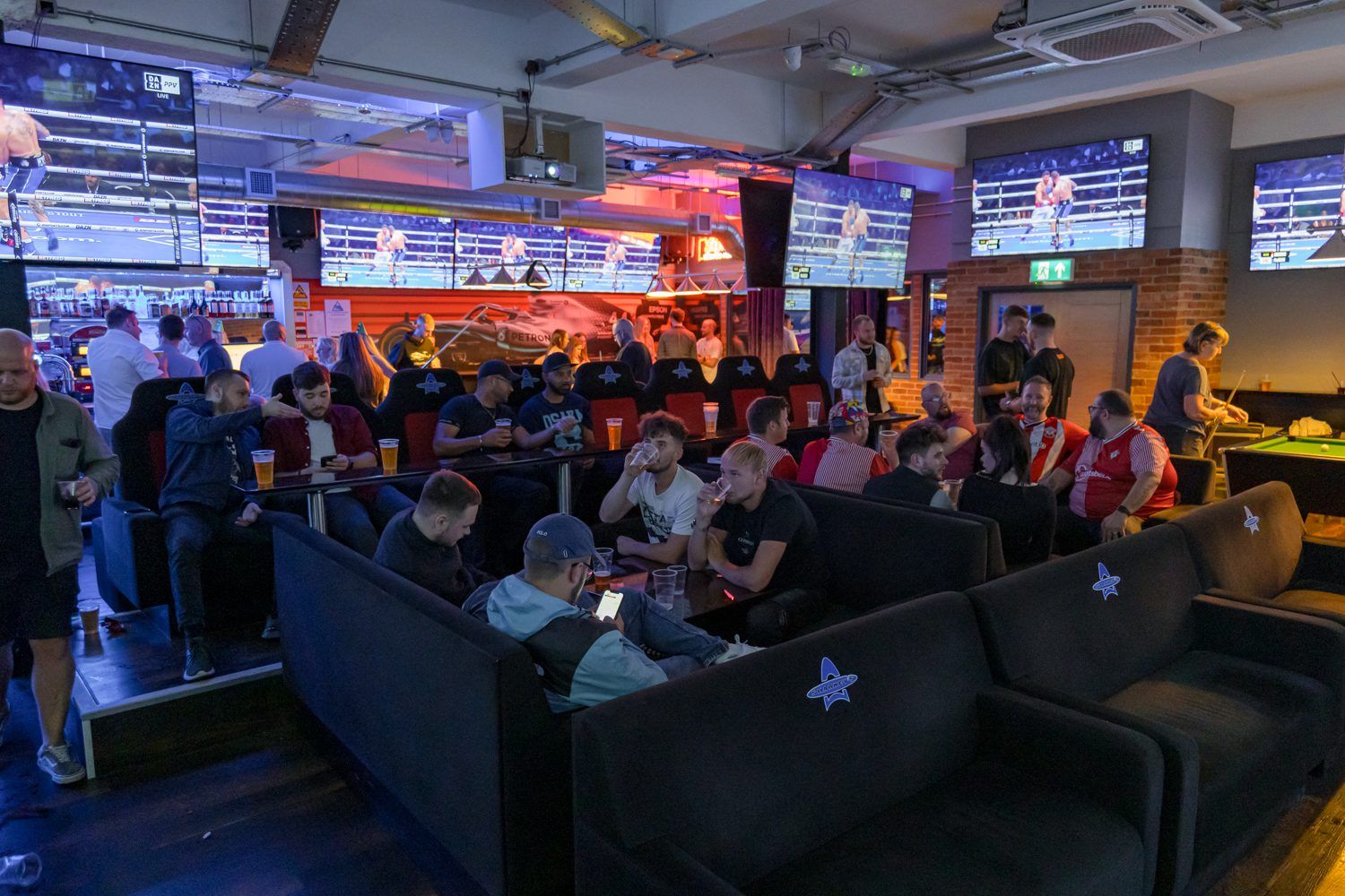 Multiple males sitting in sports bar watching screens