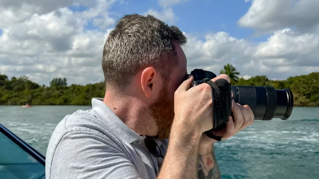 Male taking photo on boat with sea and coast behind