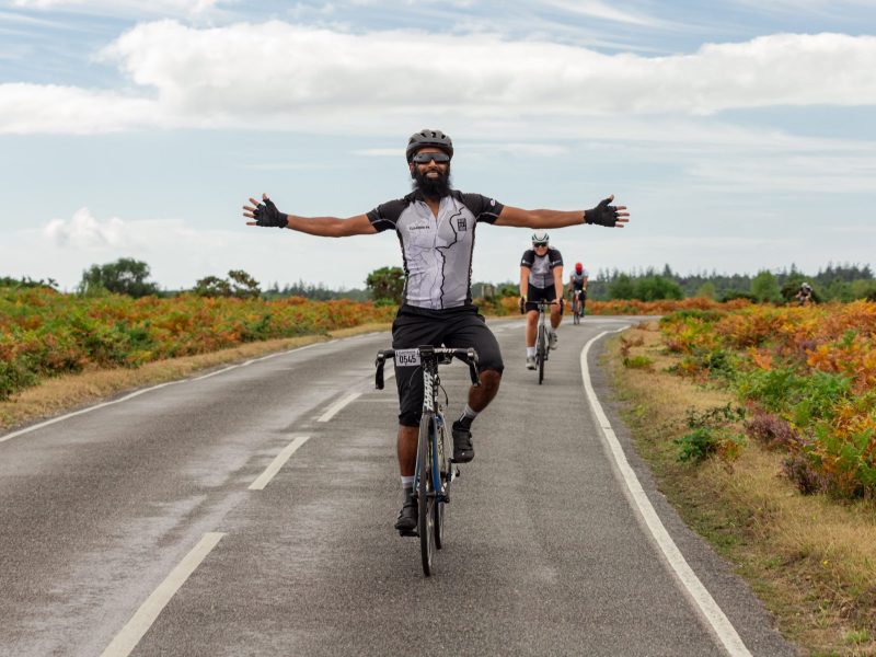 Male cyclist with arms held wide while riding bike along heather lined road